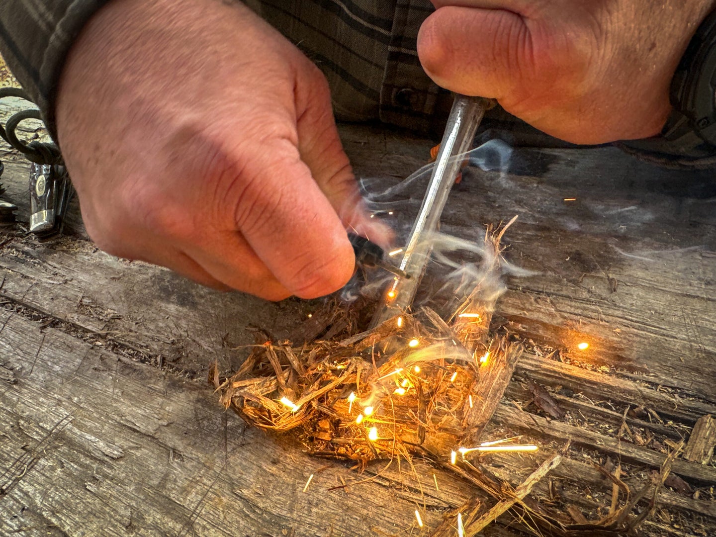 Using a ferro rod to spark fire onto a bundle of tinder