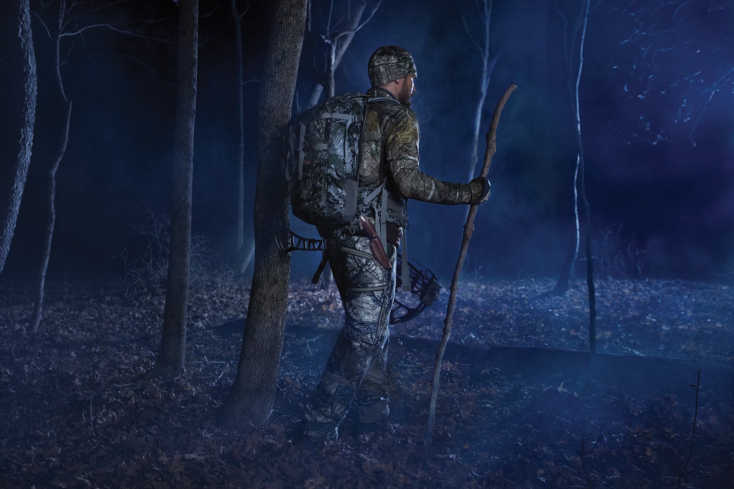 camo-clad hunter hikes through woods in long before dawn