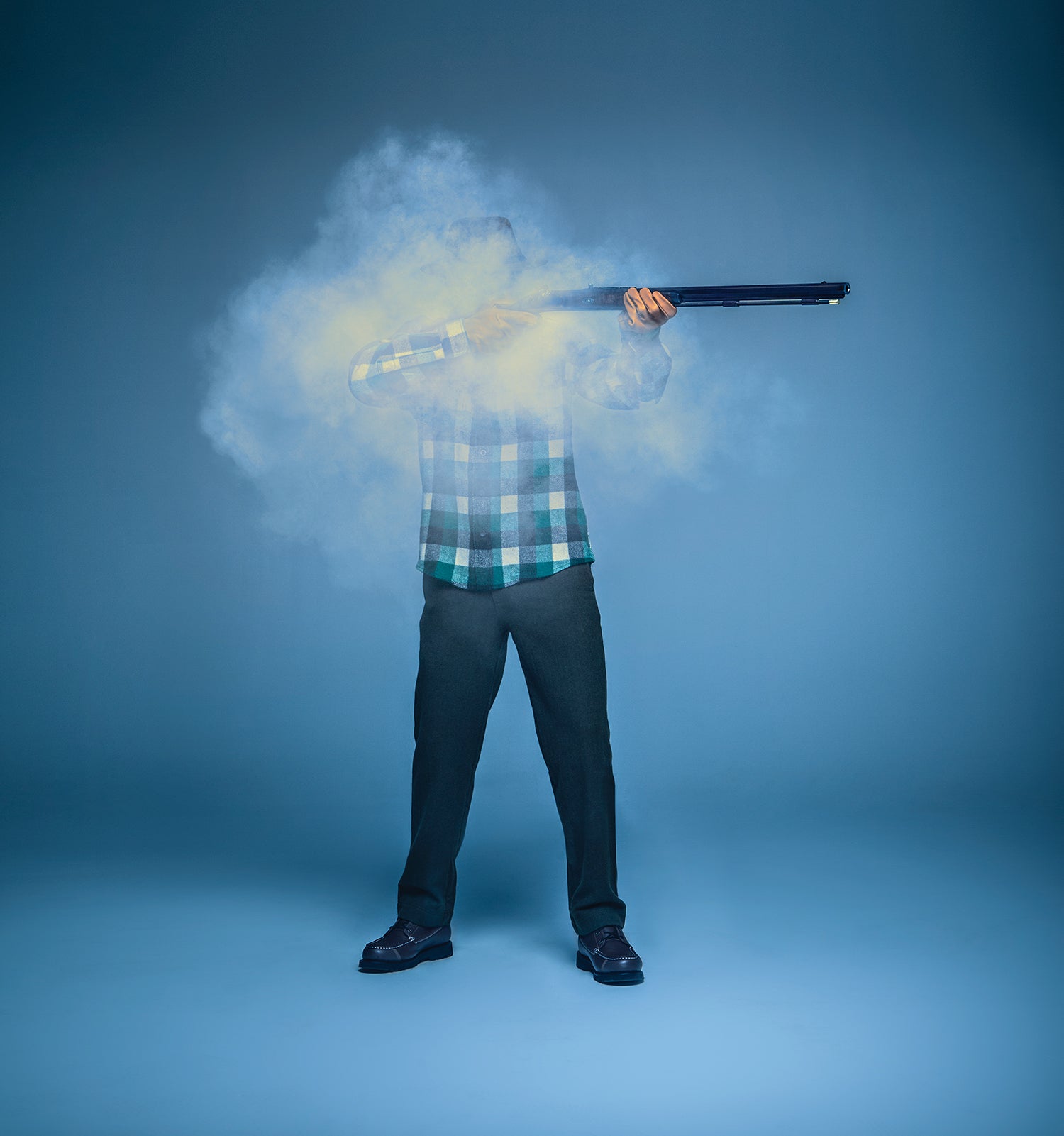 man in plaid shirt holds gun and is obscured by puff of gunsmoke