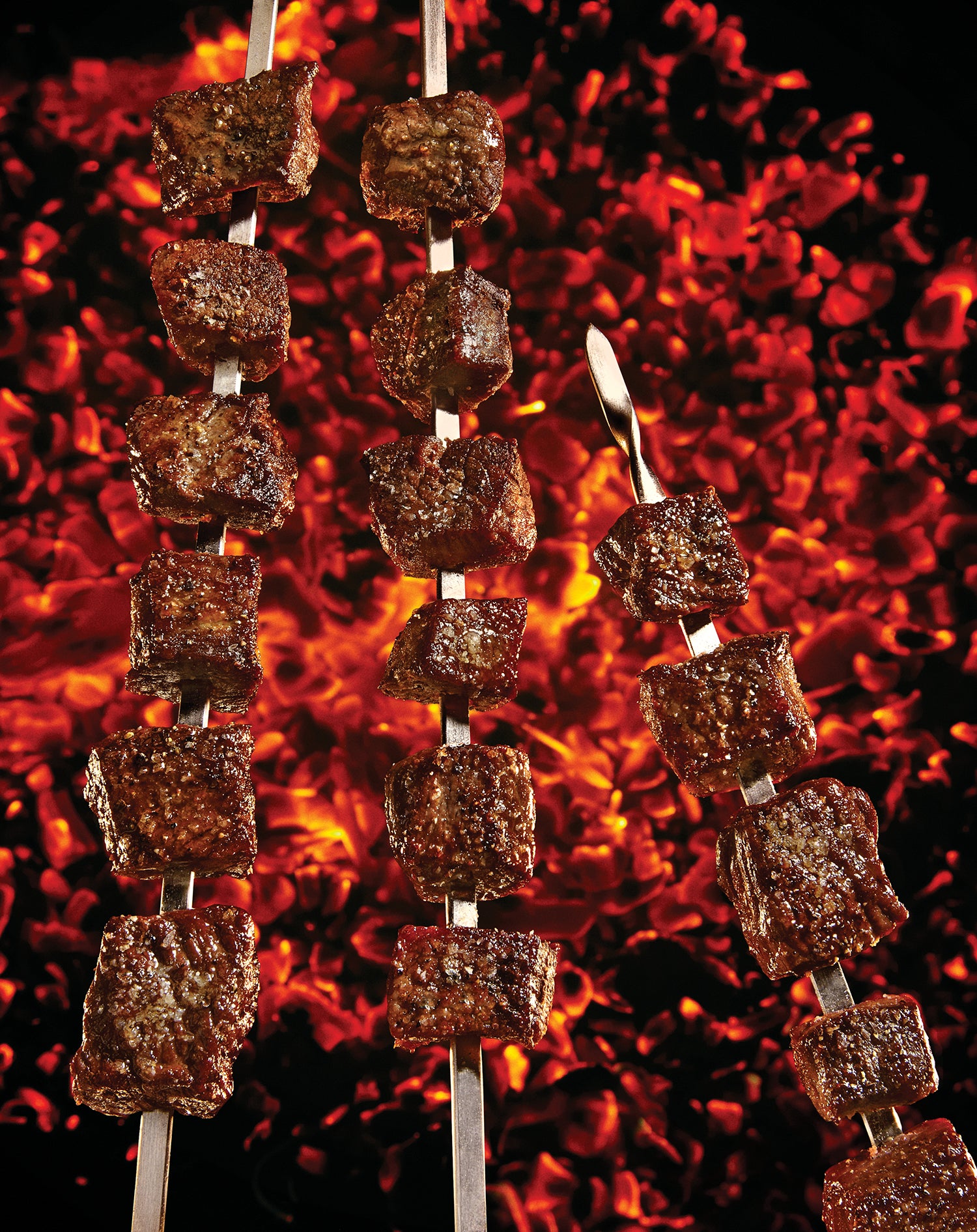 cubes of meat on skewers cook over hot coals