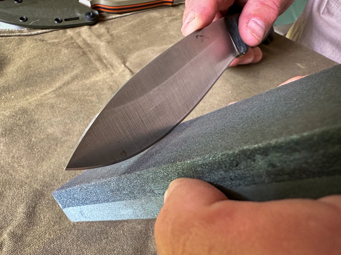 A man uses a stone to sharpen a knife