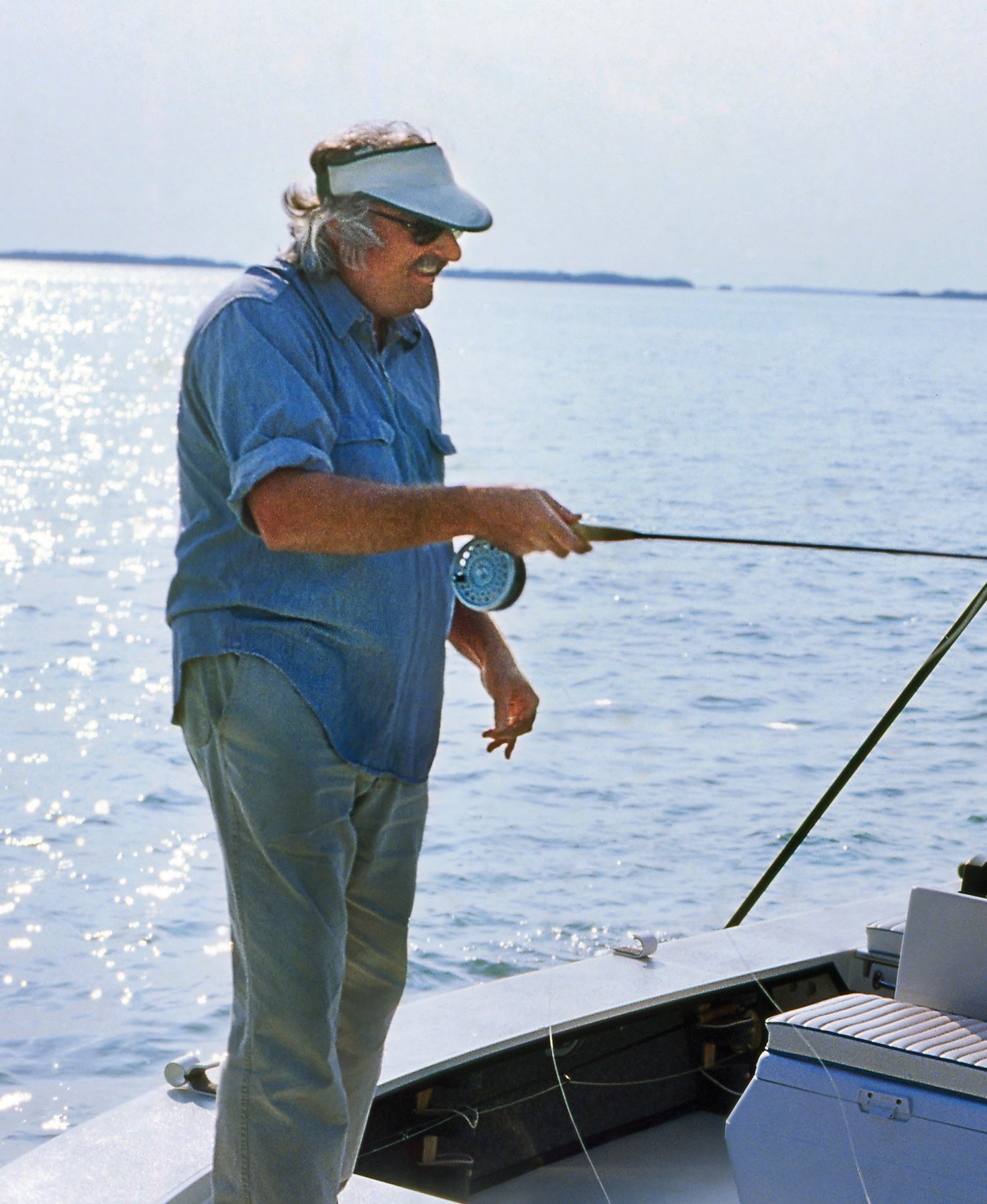 Standing on boat, Russell Chatham holds fly rod