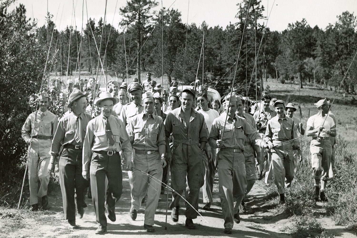 group of US airmen holding fishing rods walk down small road