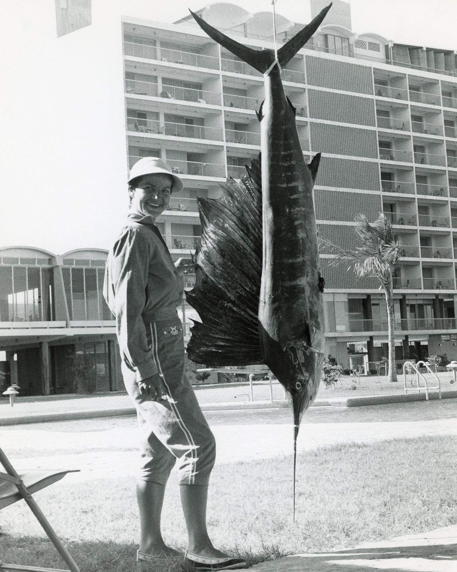 woman poses next to sailfish hanging in front of pool outside hotel