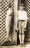 young boy holding fishing rod poses with large redfish that is only a bit shorter than he is