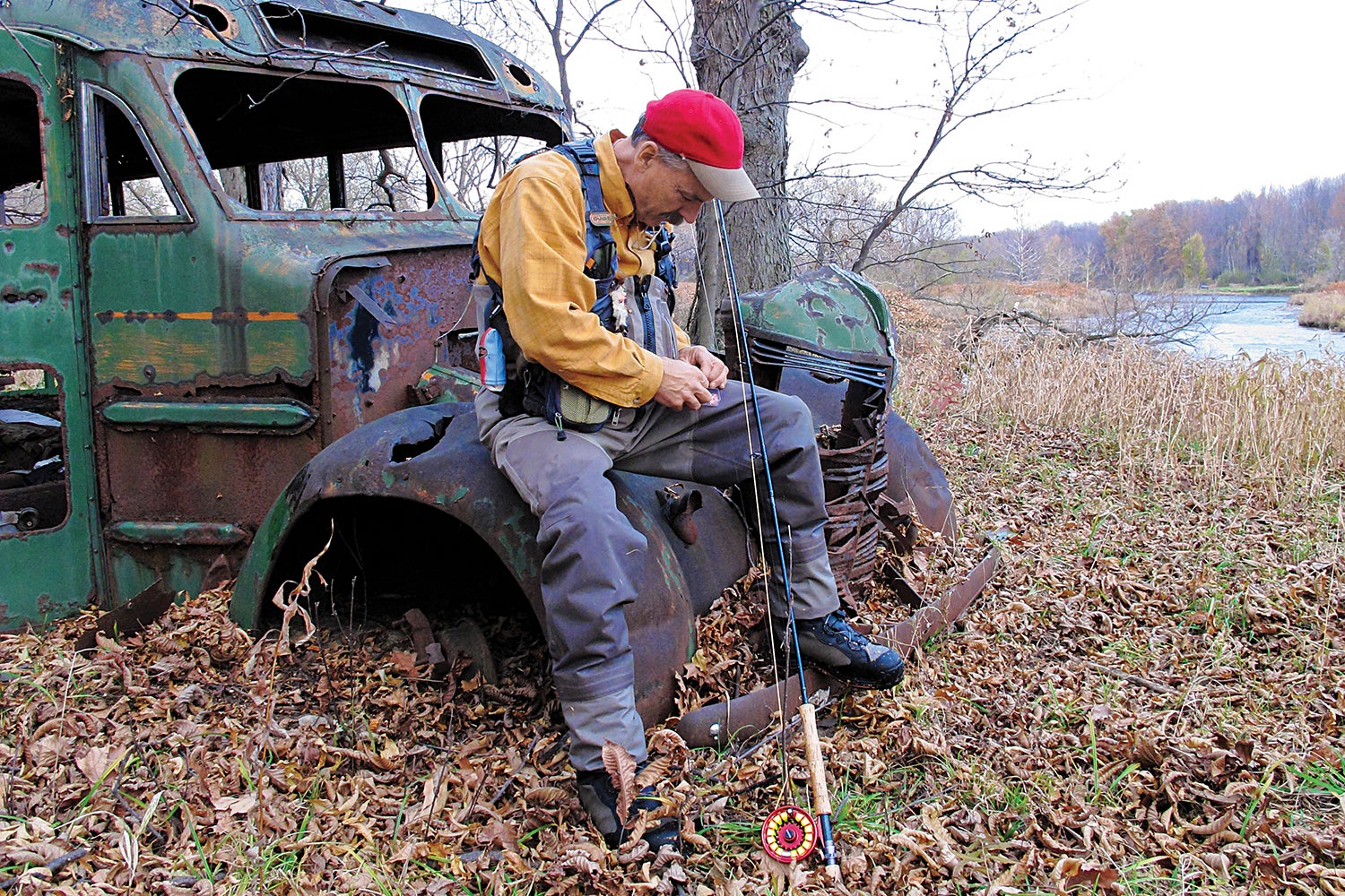 Angler sits on rusted-out bus to tie a fly to his line.
