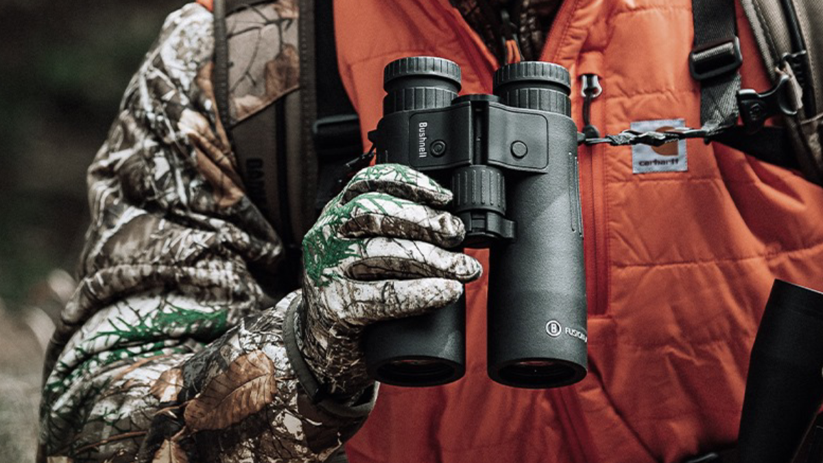 Hunter in camo and orange holding a pair of Bushnell Binoculars