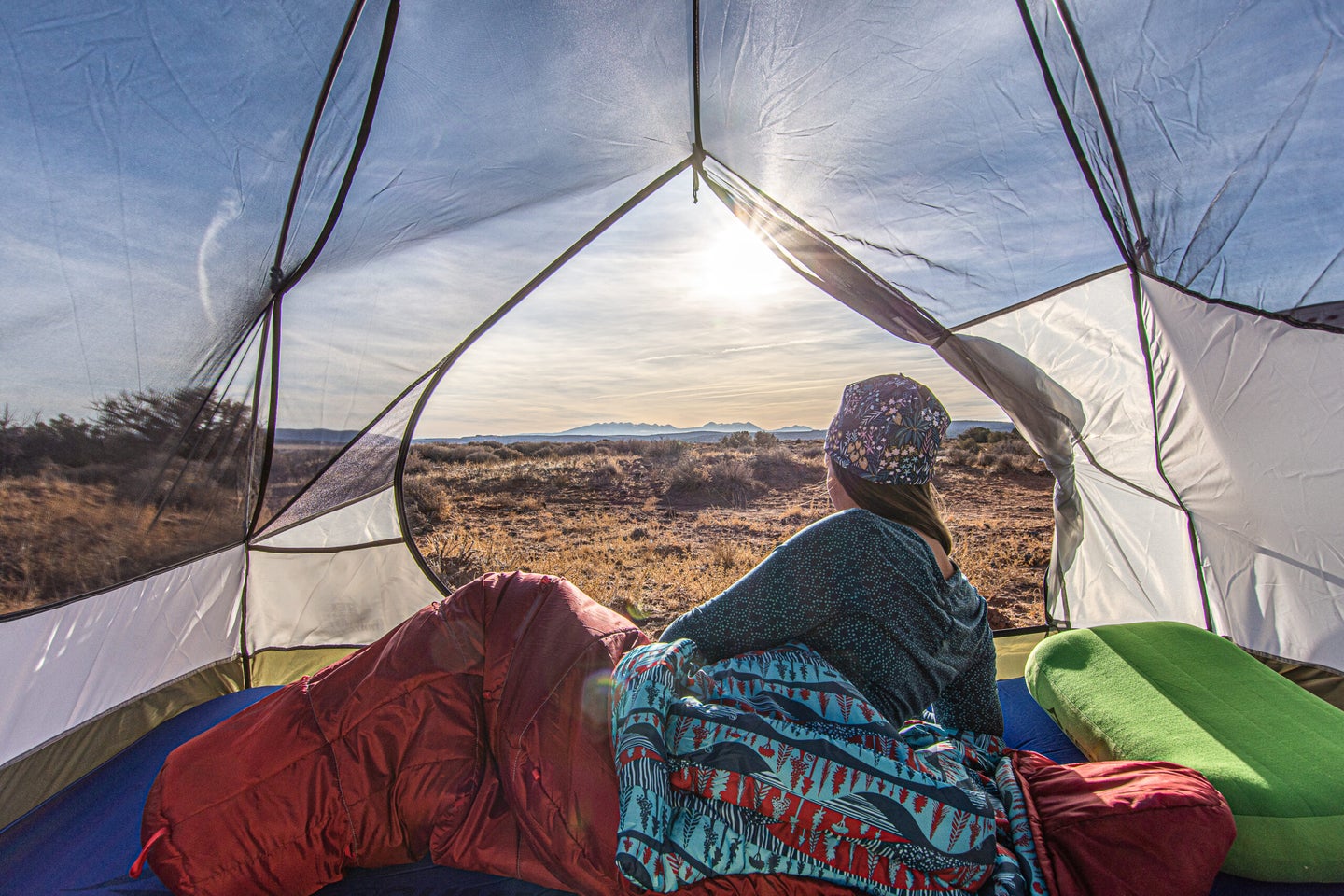 Woman watching sunrise from tent in backpacking sleeping bag