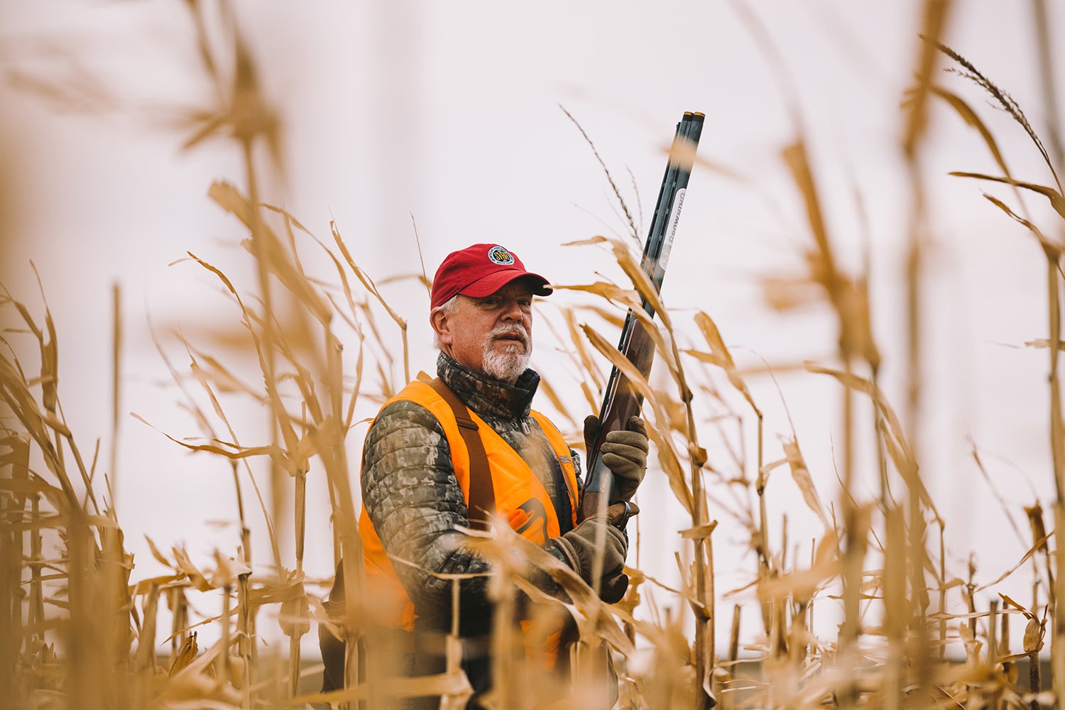 bird hunter stands in tall field with shotgun