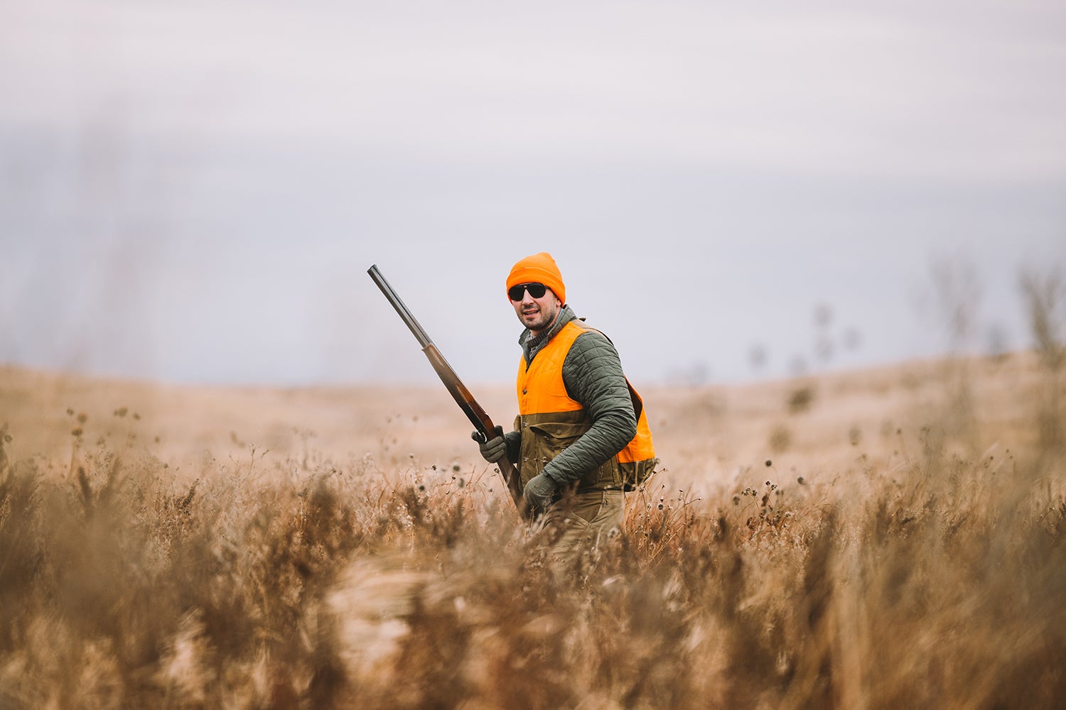 Bird hunter in orange hat and vest stands in field.