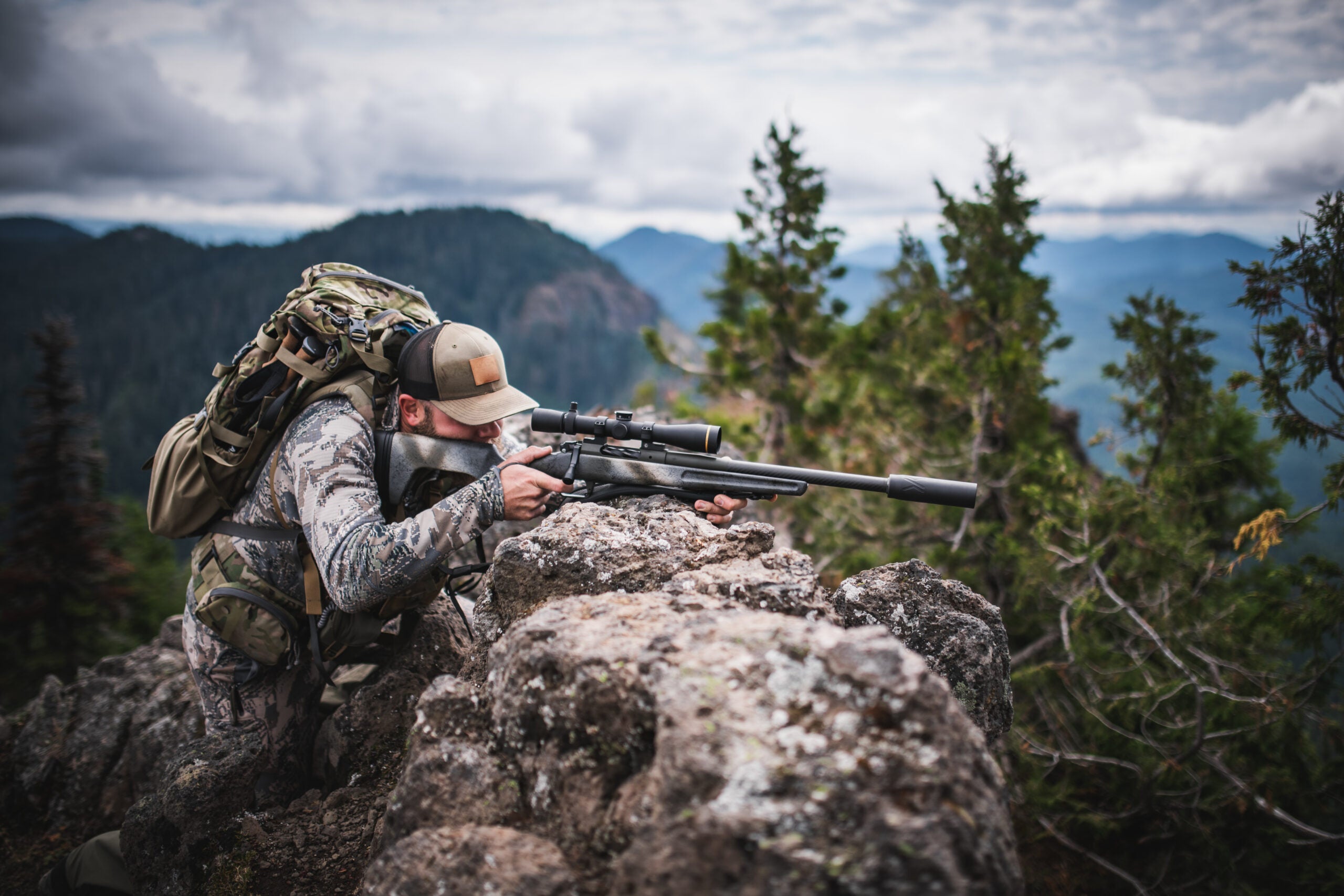 a hunter in mountainous terrain shooting a rifle equipped with a silencer or suppressor