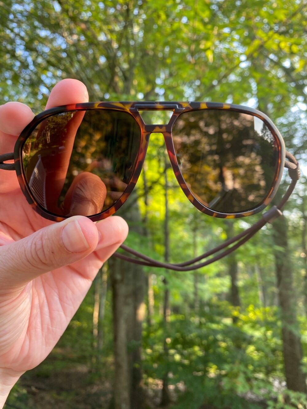 Woman holding up pair of Ombraz Classic armless sunglasses for hiking
