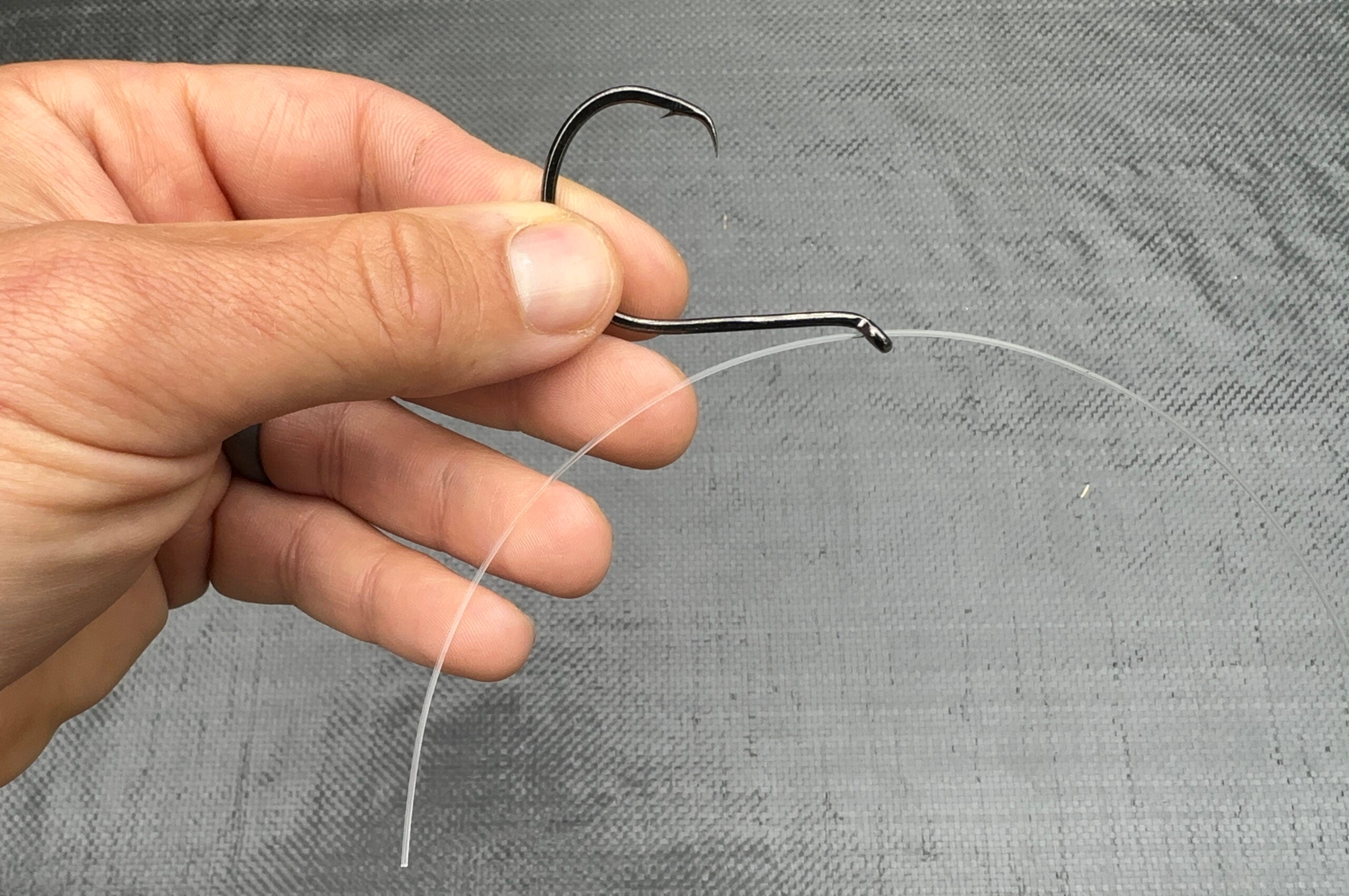 The first step in threading fishing line through a fishing hook to snell a hook