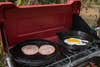 ham slices and eggs cooking on a camping stove. breakfast sandwiches are a great camping food idea