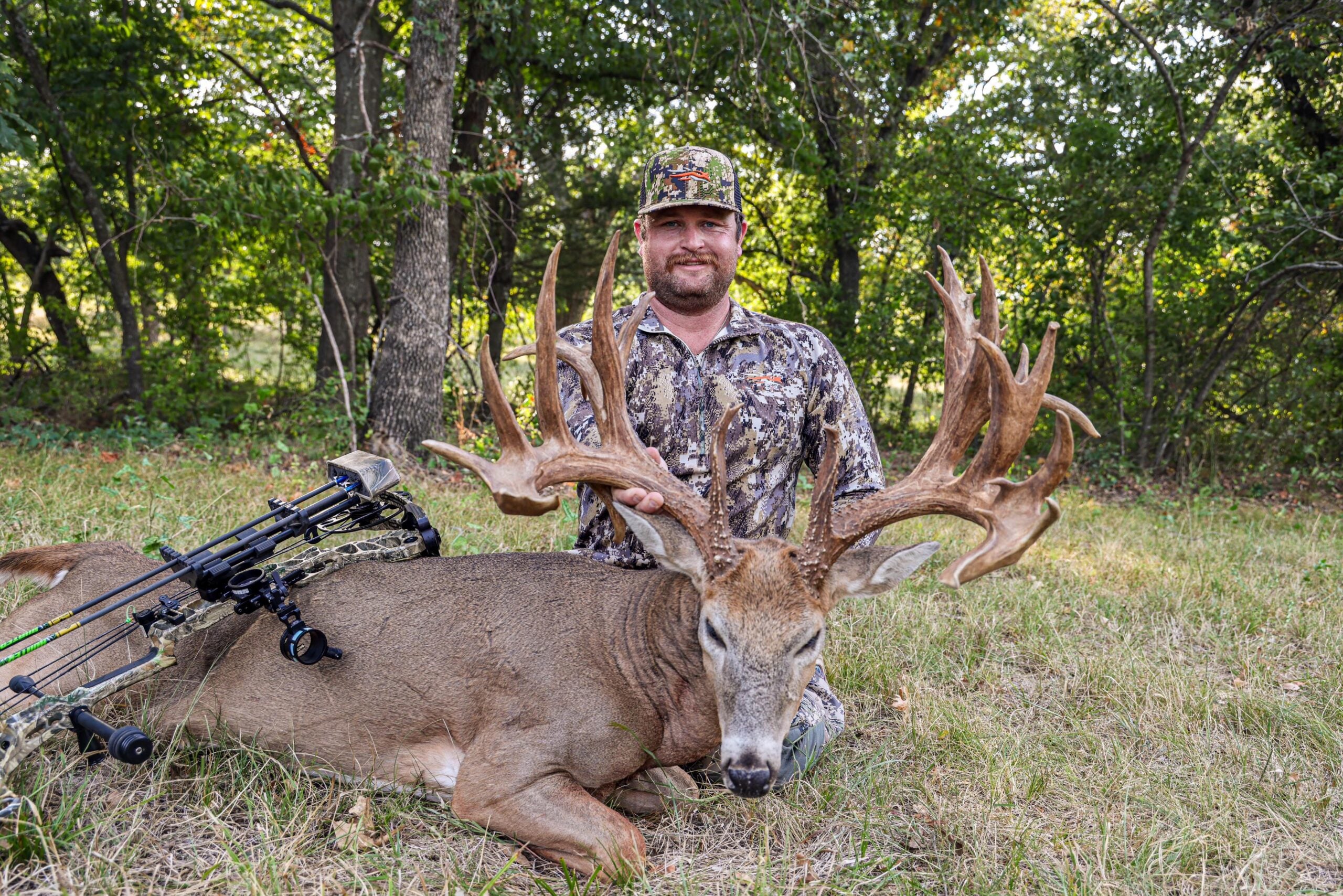 An Oklahoma bowhunter sits on the ground posing with a 200-class Oklahoma nontypical whitetail buck.