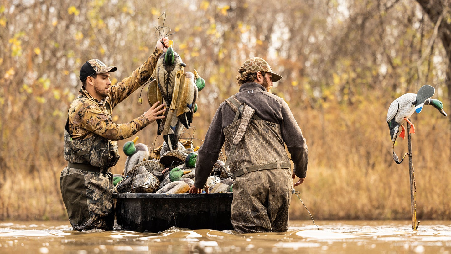 two hunters standing in pond load decoys into a small boat