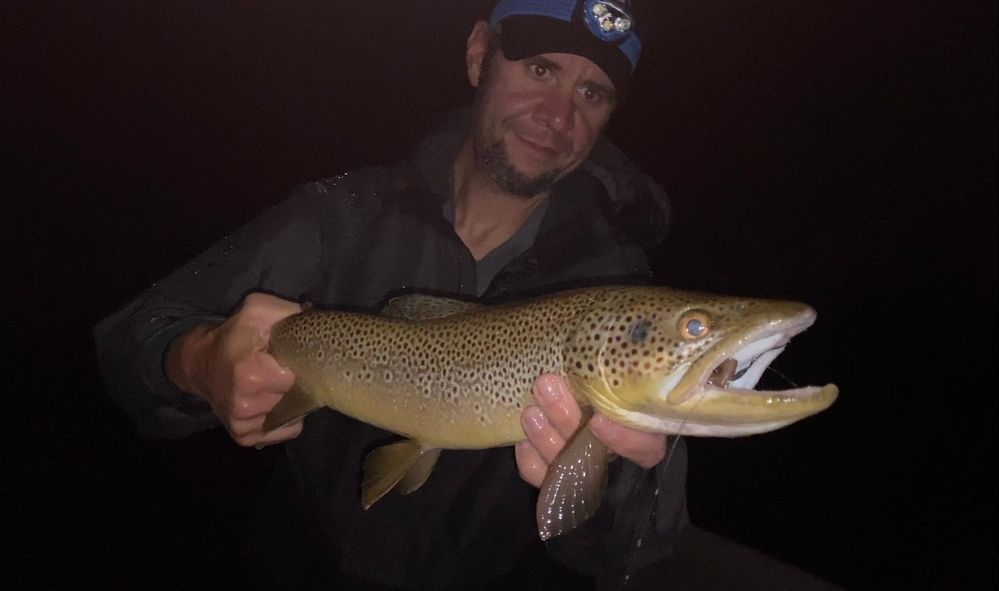 a fisherman holds a brown trout caught in fresh water at night