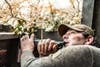 hunter peers up out of blind as he holds duck call to his mouth