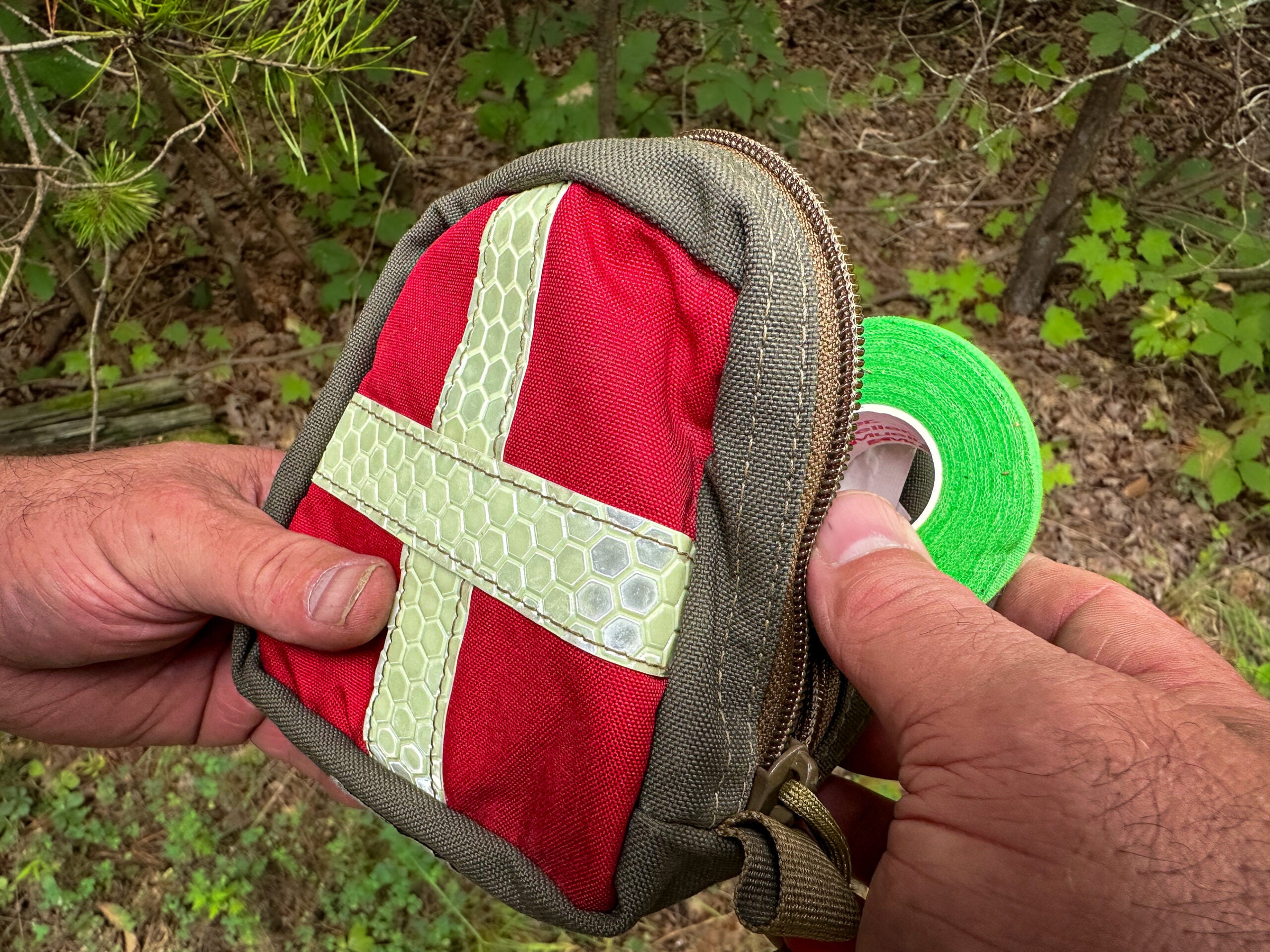 A small first-aid kit in a red bag with a white cross on it, and a roll of green tape.