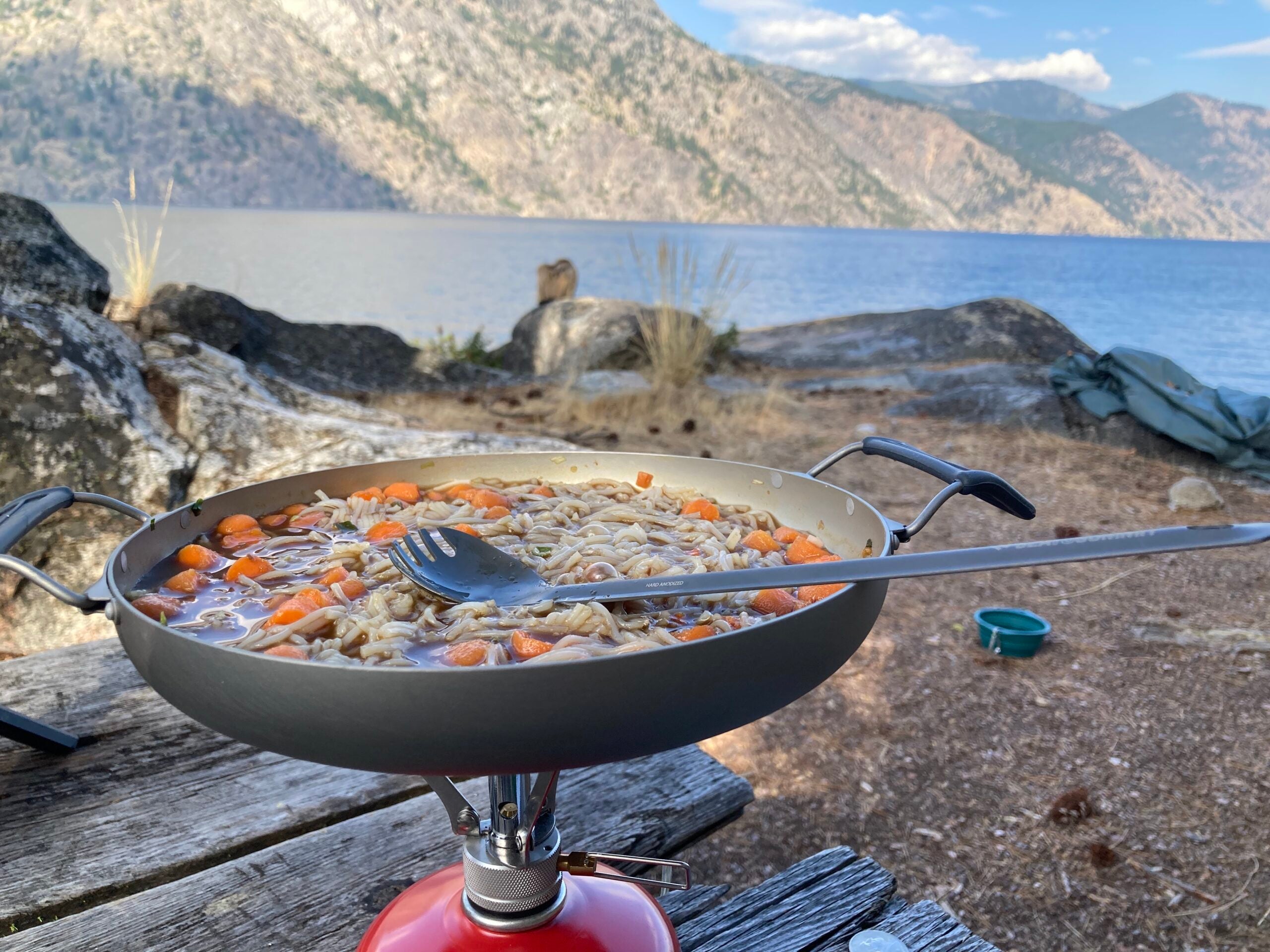 A frying pan with rice and vegetables cooking over a camping stove.