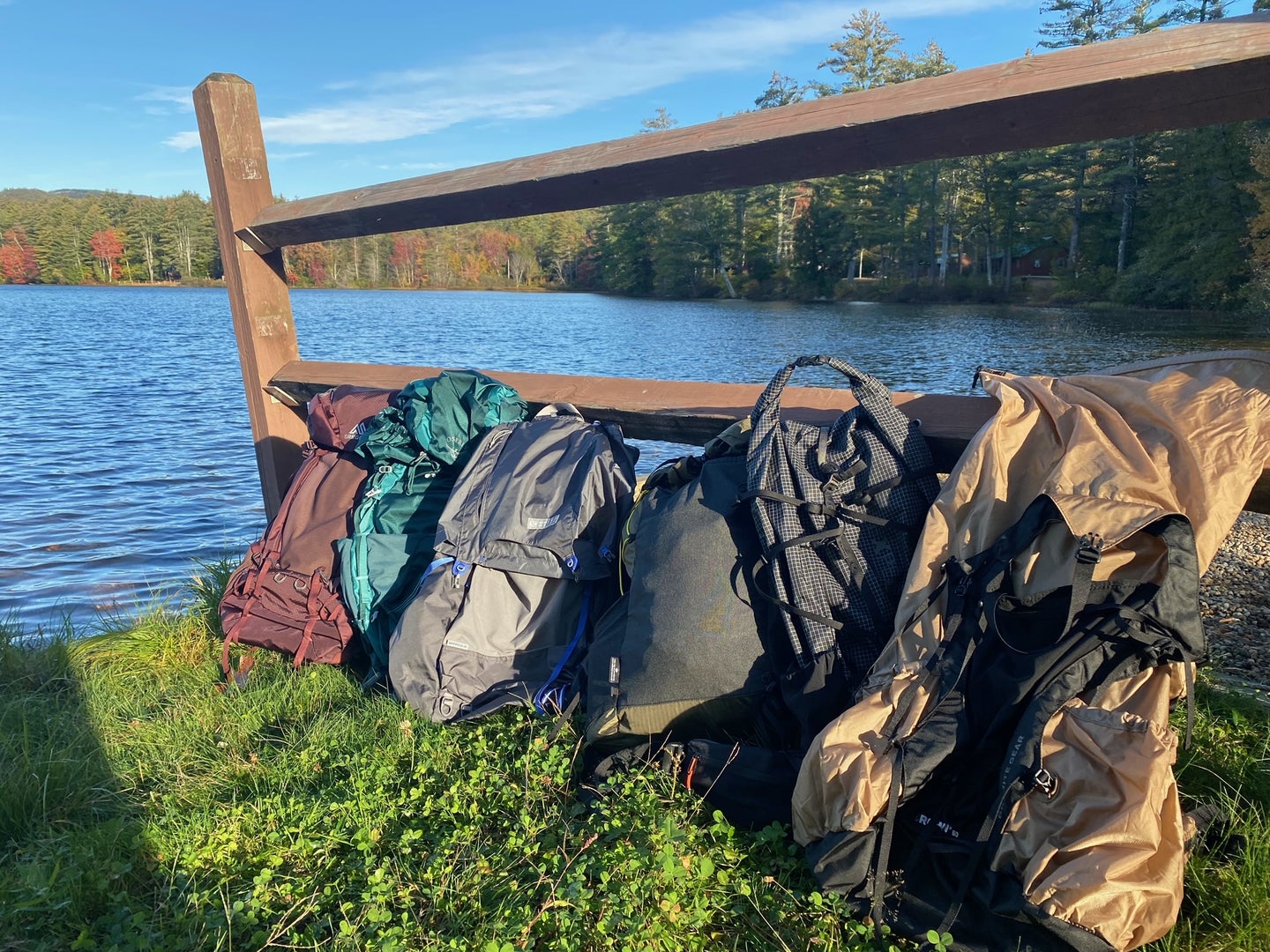 a line of backpacks leaning on a wooden fence next to a pond