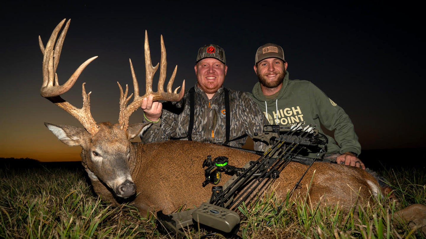 Two hunters post with a 190-class Missouri whitetail buck at night in a field.