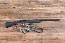 The new Benelli M2 shotgun lying on old barn boards with duck calls and lanyard nearby.