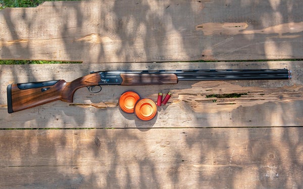A Fabarm Elos D2 RS over/under shotgun on a table with shells and two clay targets
