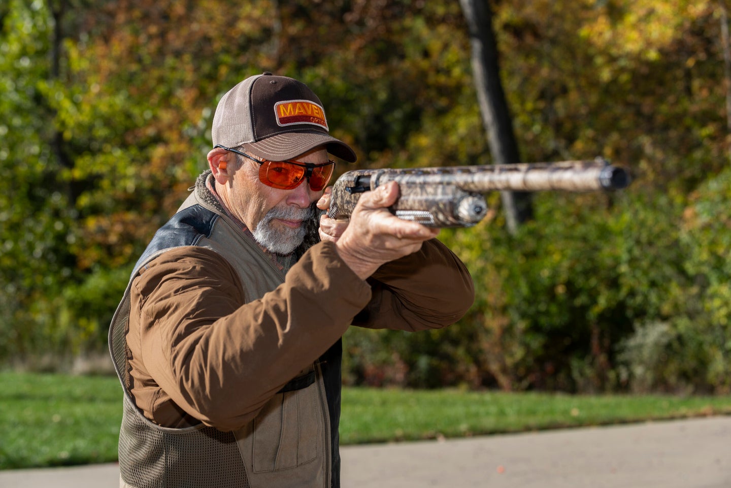 Man in shooting jacket and glasses, testing a semi-automatic waterfowl shotgun at a gun range.