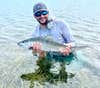 guide nick castillo stands in water and holds up a bonefish as he balances his fly rod over his shoulder