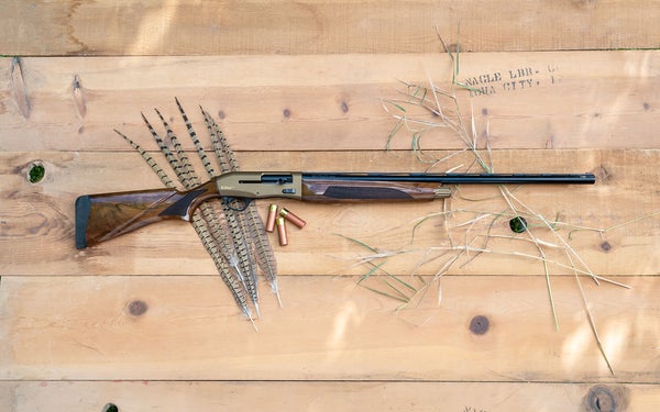 A Tristar Viper G2 Pro shotgun lying on a table with shotgun shells and pheasant tail feathers.