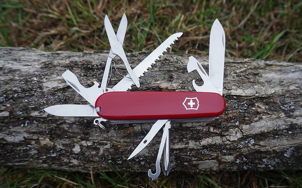 A Victorinox Swiss Army Fieldmaster knife with various tools unfolded on a grey log in the green grass.