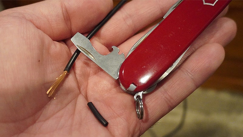The screwdriver and wire stripping tool of a white Swiss Army knife next to a black wire in the palm of a hand. 