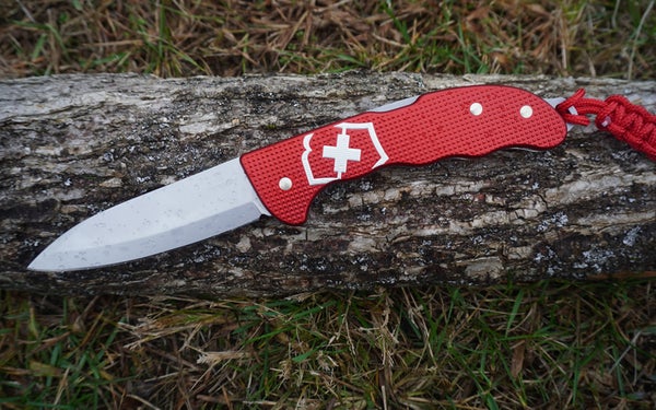The red and white Swiss Army Hunter Pro folding knife sitting on a grey cut log on grass.