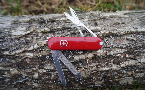 A red and white Victornox Swiss Army Classic SD sitting on a grey piece of firewood.