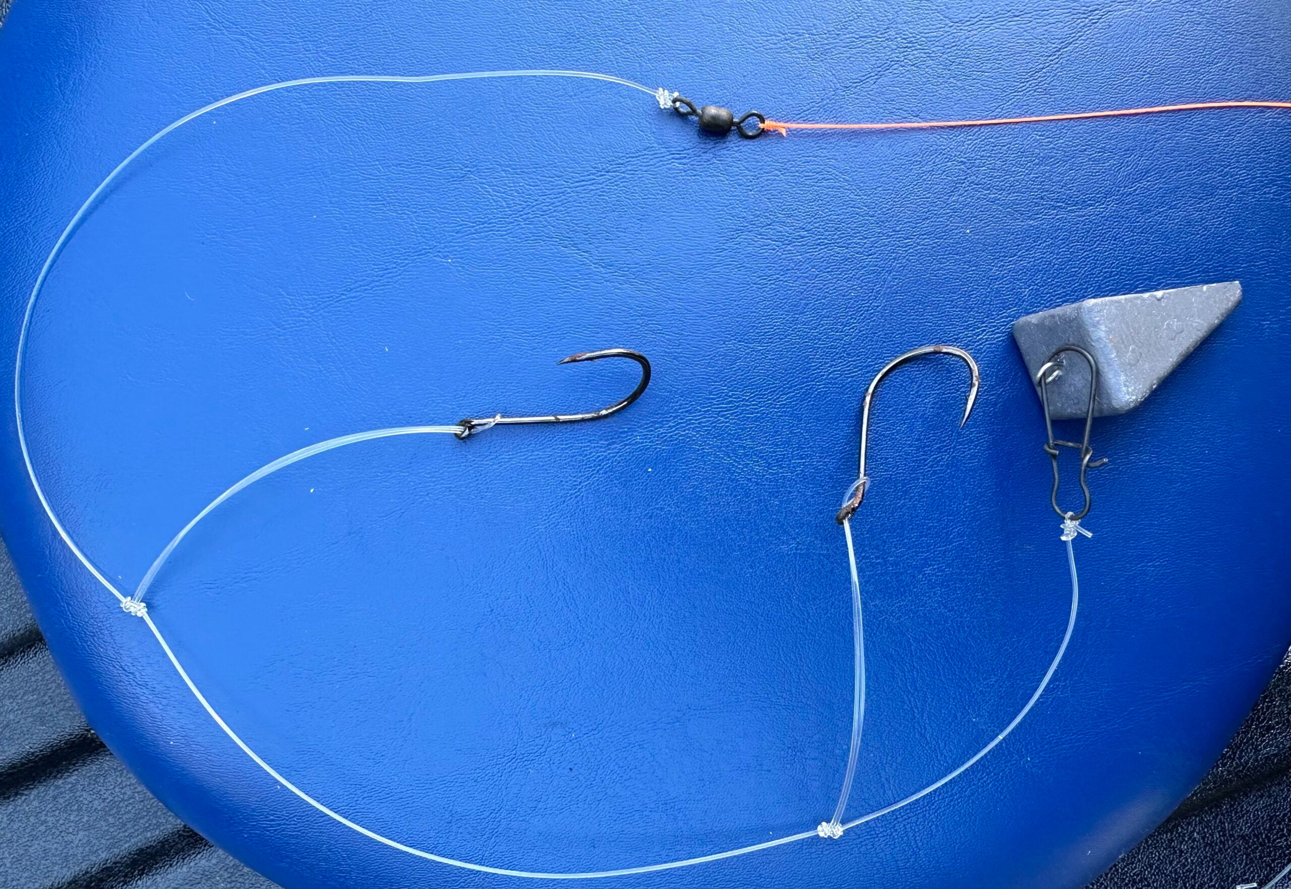 A high and low surf fishing rig, tied with a pyramid sinker, fishing hooks, and fishing line, shown on a blue background.