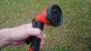 The red and black nozzle of a hydropod shower being held in front of a green grass background. 