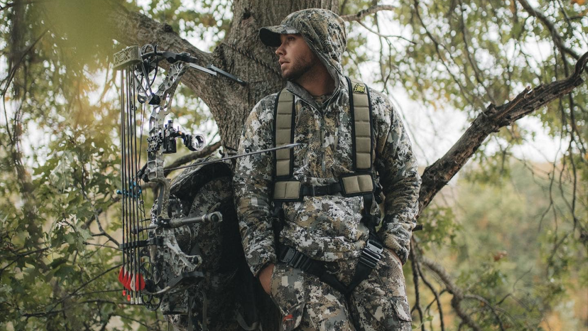 Hunter wearing Sitka jacket and pants in tree stand with compound bow