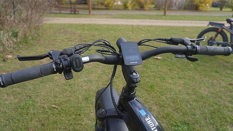 The black handlebars of an electric bike against a grassy background. 