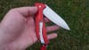 The red and silver Swiss Army Alox knife being held in a hand above a grass background. 
