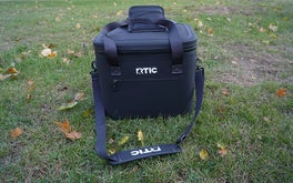 The black RTIC soft pack cooler on a green lawn.
