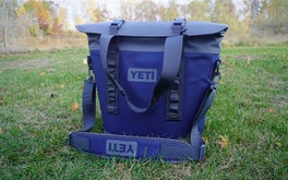The dark blue and gray Yeti M15 cooler and shoulder strap on a grassy lawn.