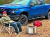 Camper sitting next to fire pit and generator with blue truck in the background