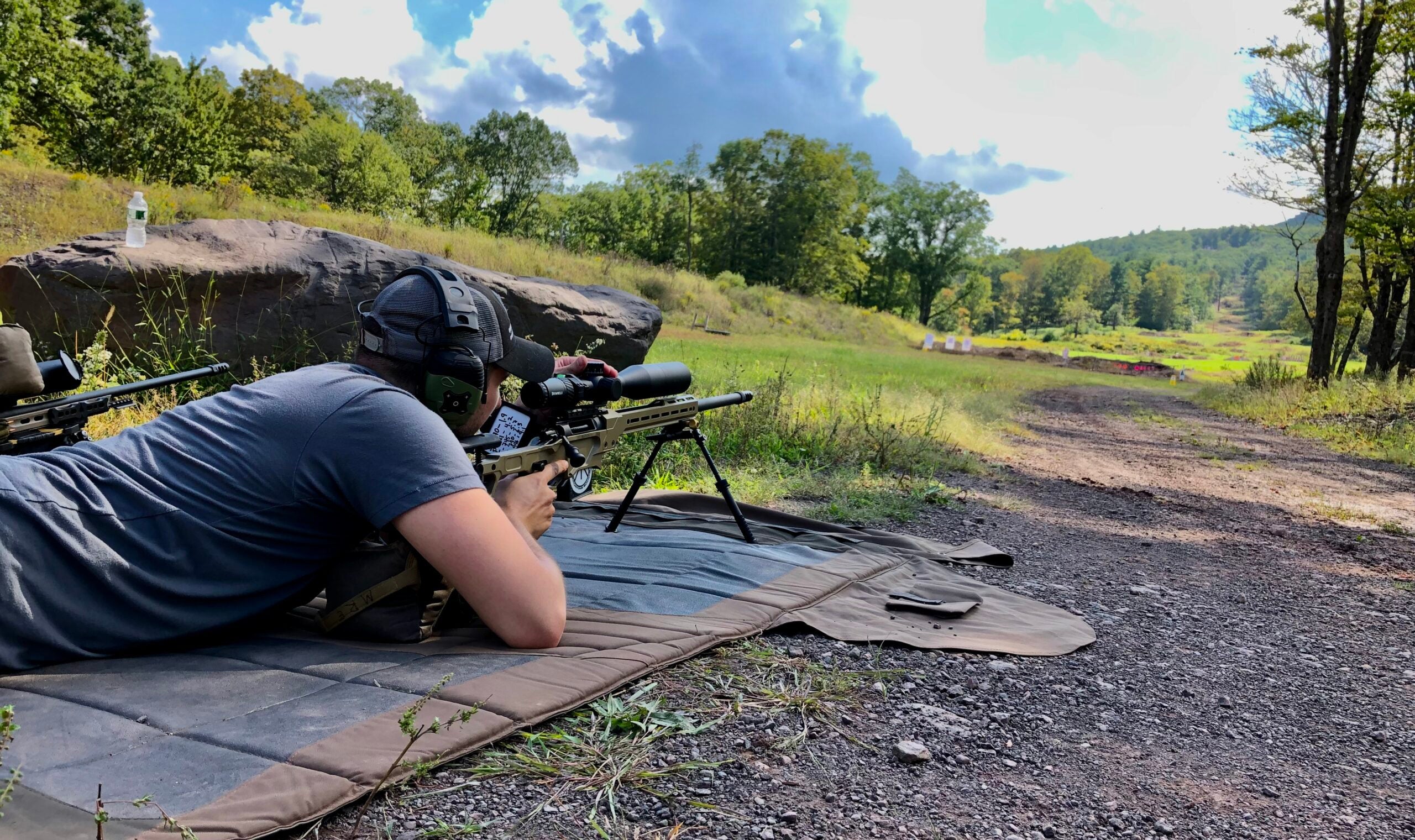 A shooter laying down on a pad behind a rifle adjusts his MRAD scope at a long-range shooting match