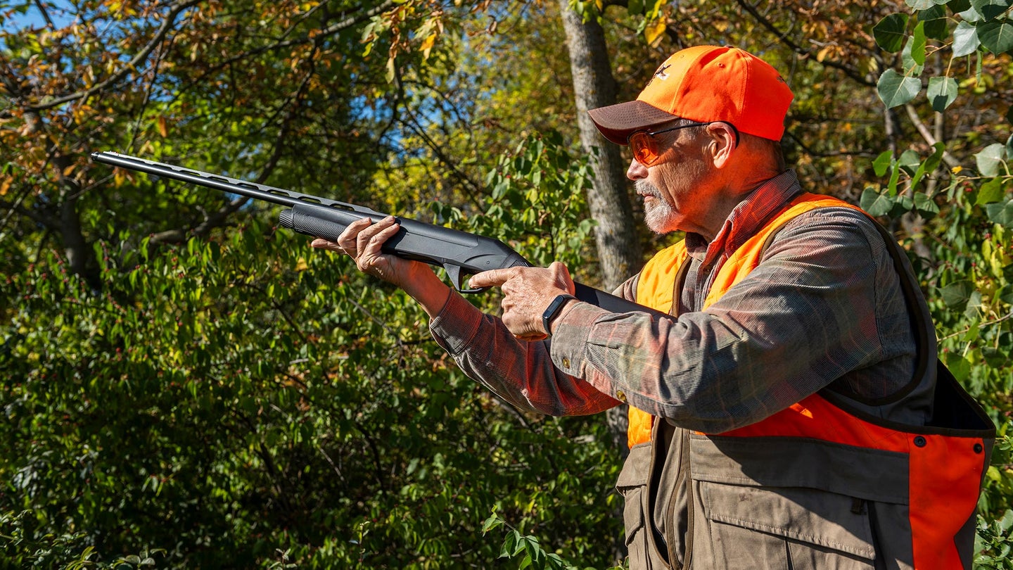 bird hunter in orange hat and vest raises shotgun