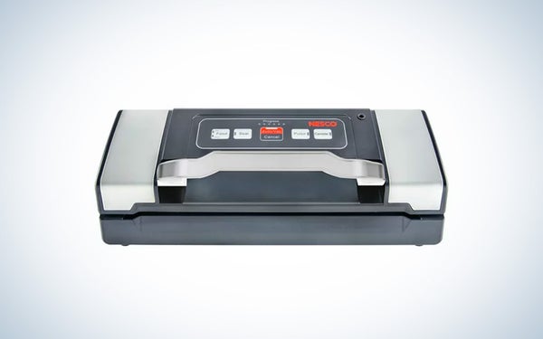 A silver and black vacuum sealer with white and red buttons sitting on a black and white gradient background.