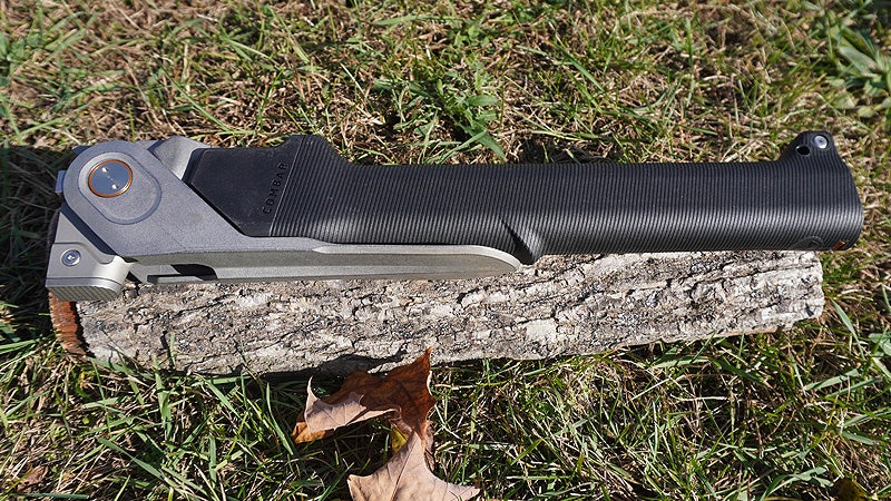 A black and silver Combar multi-tool sitting on a log on a grassy lawn. 