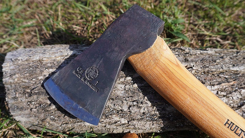 The black and silver head of a Hults Bruk Almike axe sitting on a log on a grassy lawn. 