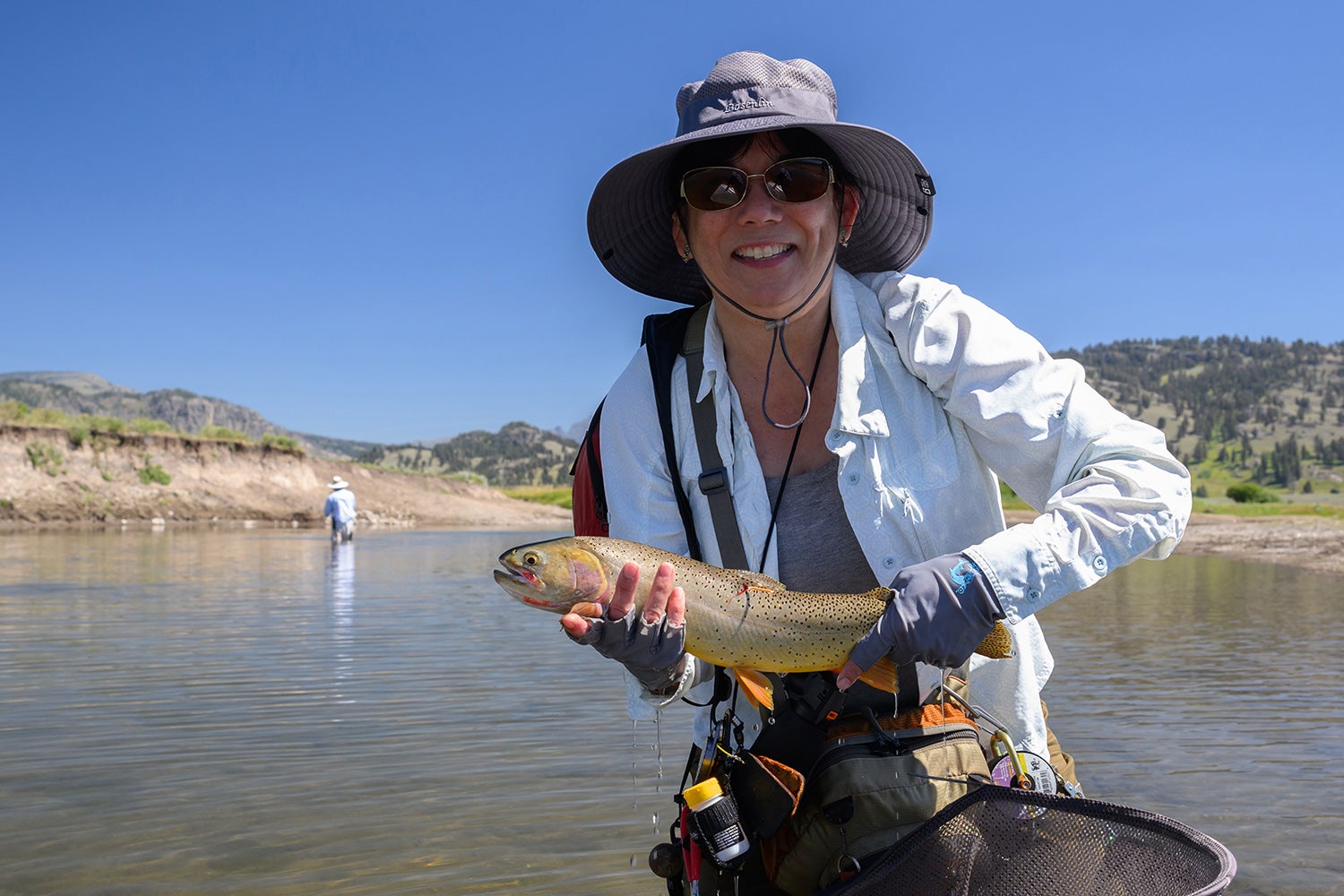 angler in river holds up cutthroat trout