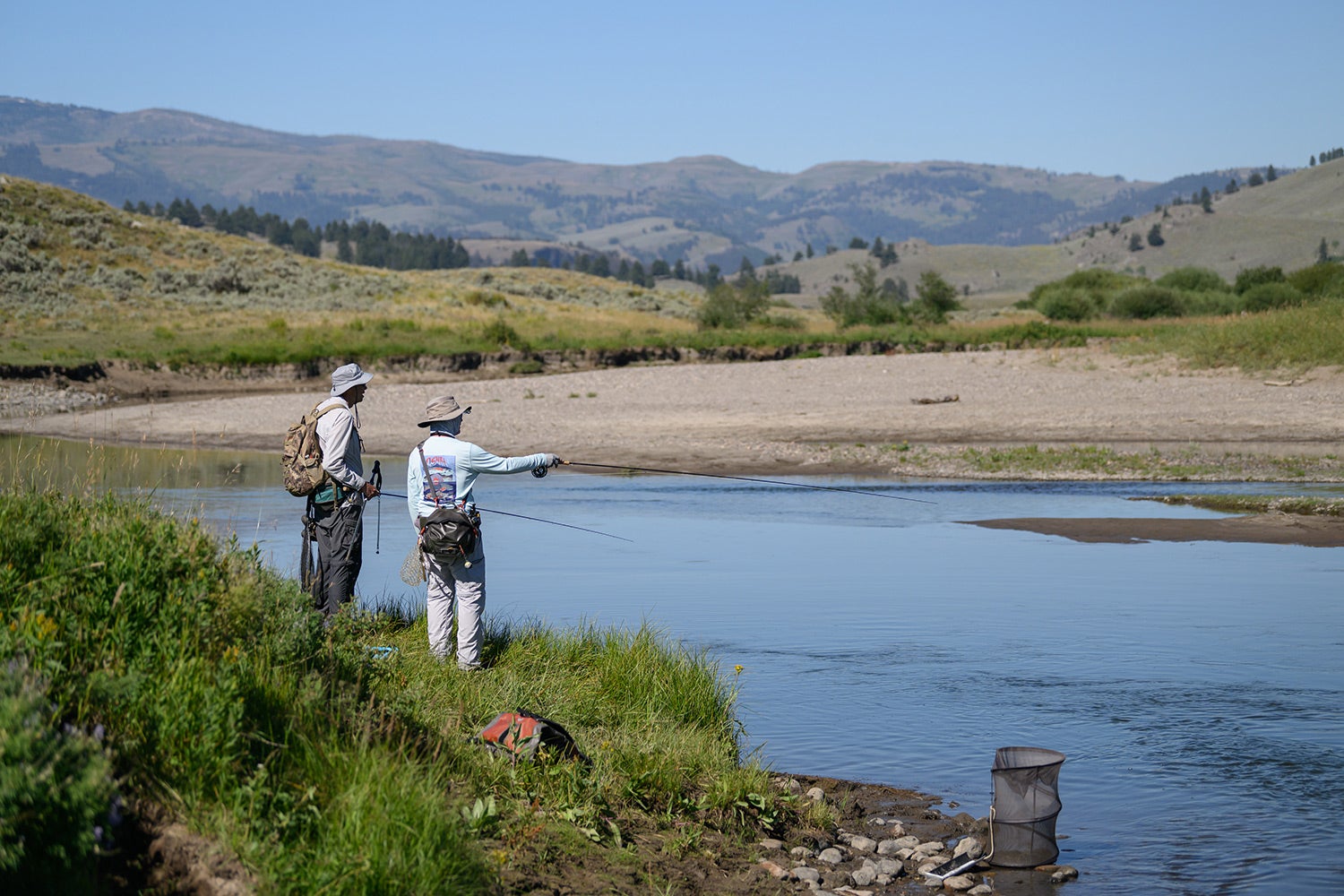 two fly anglers on riverbank in Yellowstone point their rods toward the river